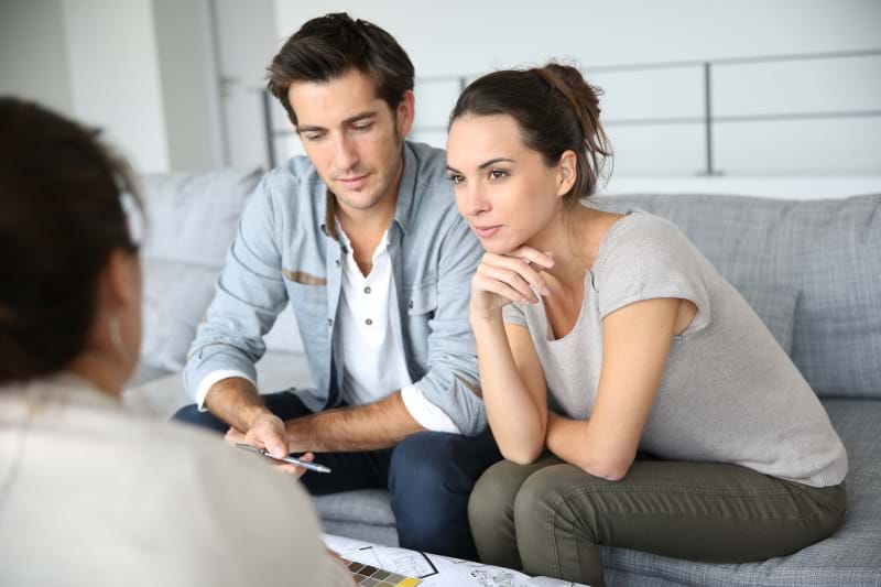 Man and woman sitting on a gray couch across from an out of focus woman